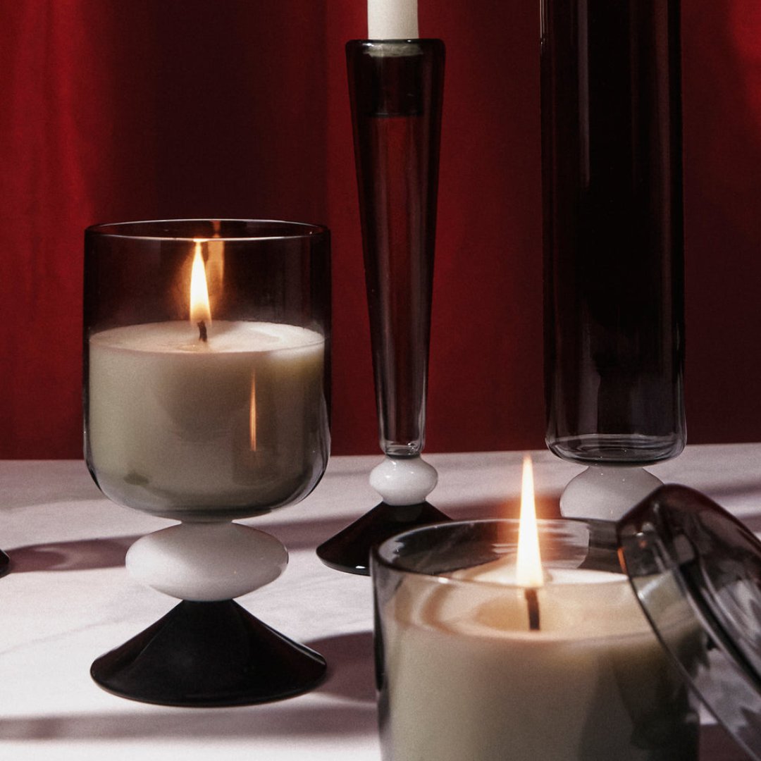 Twilight candles in black glass holders on a reflective surface with a dark background