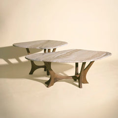 Two modern nesting maya tables with oval light beige marble tops and sculptural dark brown mango wood base, set against a warm beige background.
