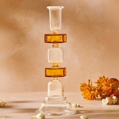 A kanak clear glass candle stand with a yellow tint, with a tapered shape, displayed on a beige surface with some decorative elements around it.