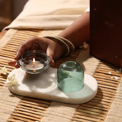 Muun Dome Tealight Holder in teal, hand placing lit slate grey base on white tray, gift box behind