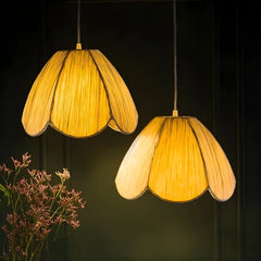 Two yellow pendant lamps handcrafted with banana-fibre paper, shade in petal-like form hanging against a dark background with a plant on the left.