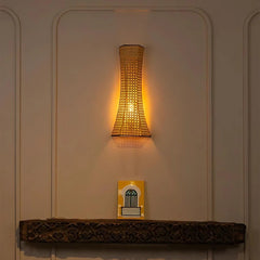 Woven wall light fixture on a neutral wall with a decorative shelf below.