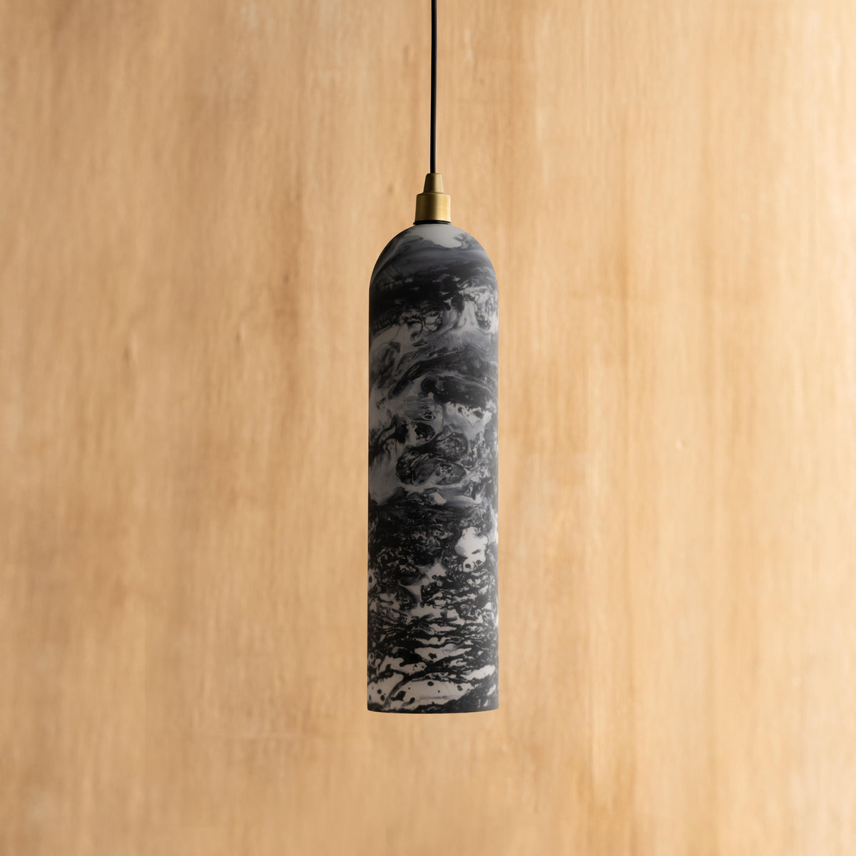 A black hanging lamp with a marble pattern, cylindrical in shape, with a gold accent at the top, suspended against a wooden background.