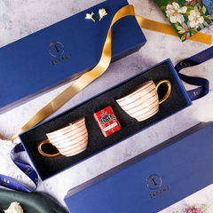 Two white tea cups with gold detailing and a tea tin, in a gift box along with the branding box