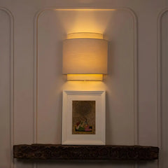 Wall-mounted lamp casting a warm glow on a wall with a framed picture below.