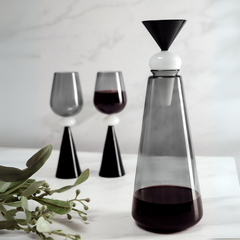 Modern glass decanter with white & black lid and two glasses on a white surface