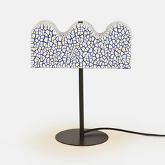 A table lamp with a black base and a ceramic white shade with a wavy blue and white pattern.