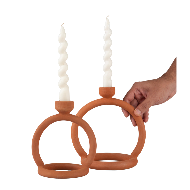 Two terracotta candle stands with cylindrical white candles, held by a hand against a white background.