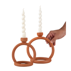 Two terracotta candle stands with cylindrical white candles, held by a hand against a white background.