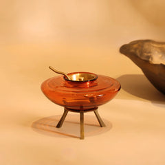 Muun Ghee Daani amber glass pot with brass lid and spoon on metal stand, angled side view