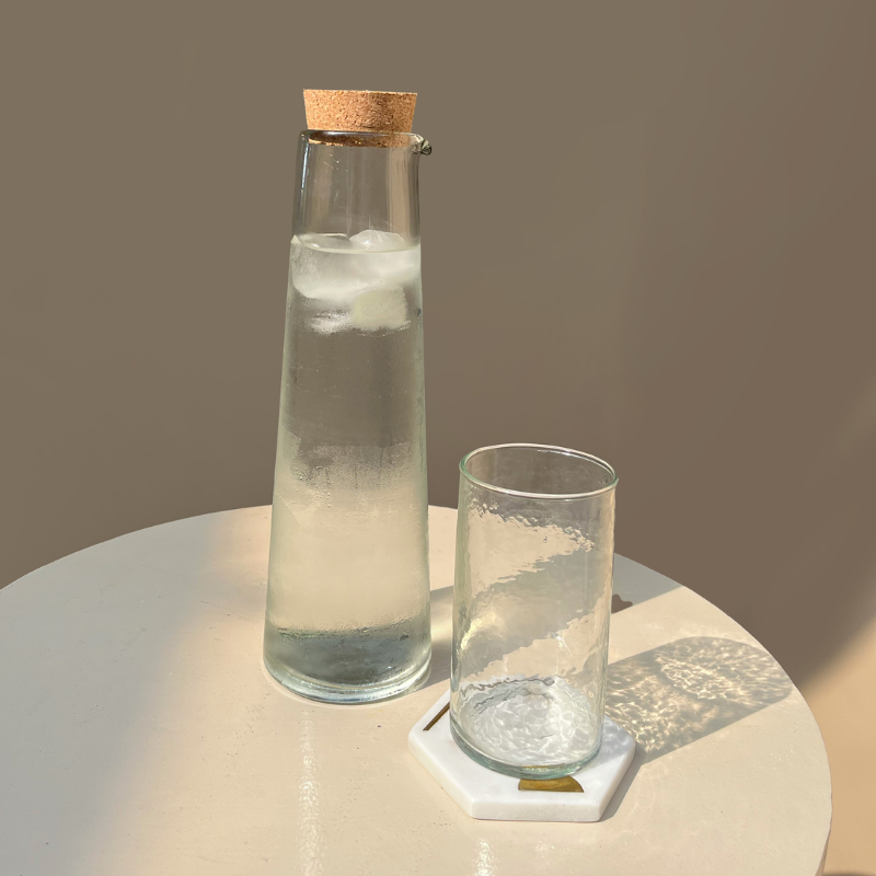 Clear glass carafe with cork lid and glass on a round surface with a neutral background