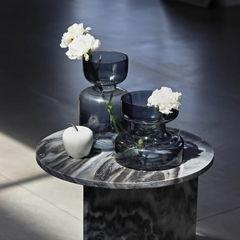 Two slate grey glass vases one tall and one small, with white flowers on a marble side table.