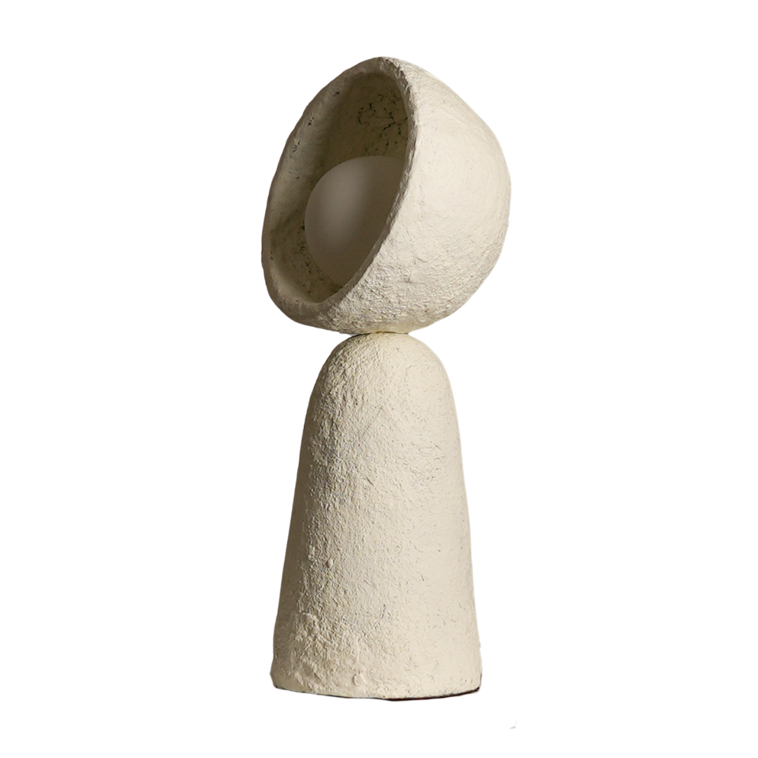 A handcrafted Echo Sphere Table Lamp made from paper mache, with a textured, beige surface. The lamp is designed with a spherical shape and a hole at the top, presumably for the light to emit from.