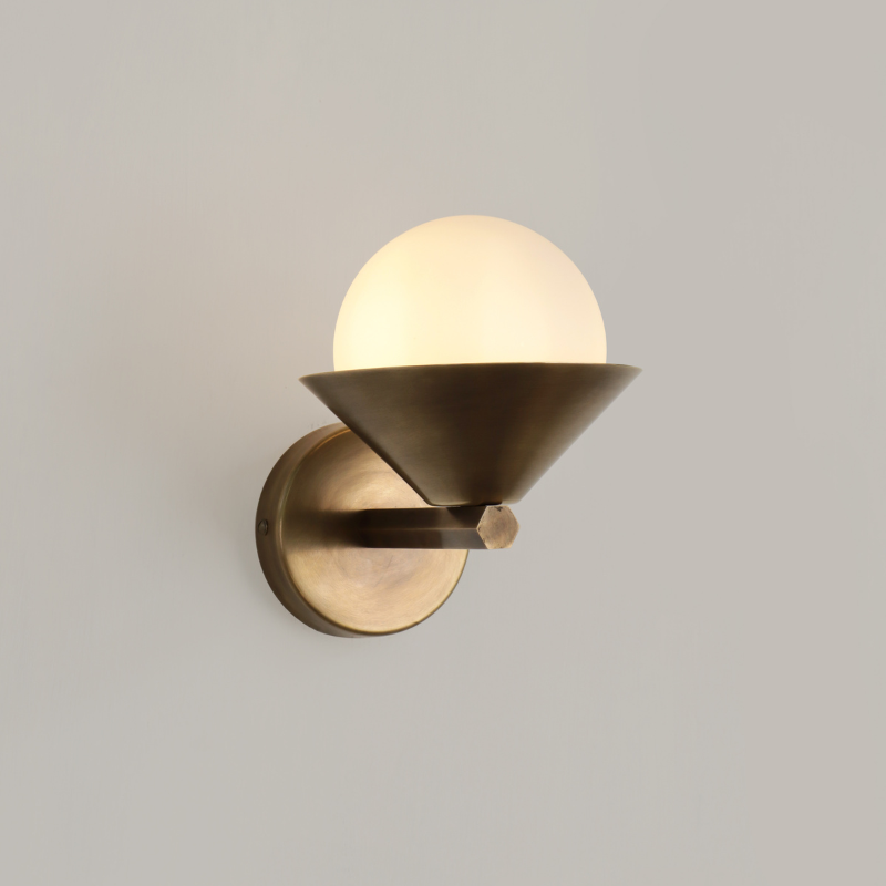 Interior view of Cone Wall Sconce One lit on wall, aged brass finish casting warm light