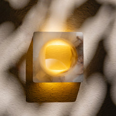Tunnel Wall Sconce featuring a square form with a meticulously carved tunnel-like cavity that filters light inwards and radiates a soft glow.