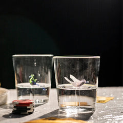 Eileen Two clear Drinking Glasses with small figurines on a dark background