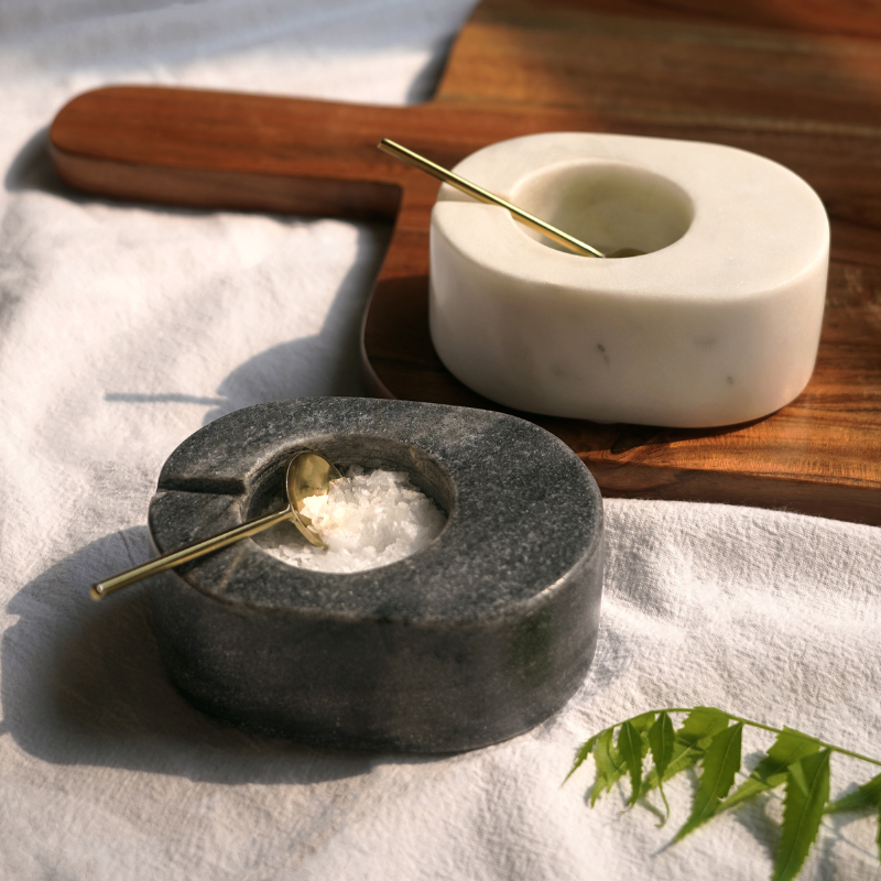 Marble spice bowls set of 2,  with metal gold color spoons on a wooden board.