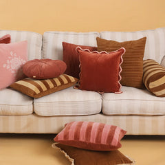 A collection of cozy decorative throw pillows in various colors and textures arranged on a cream-colored striped sofa against a warm beige wall.