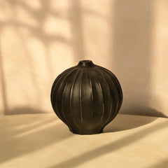 Black ribbed Opus Vase on a beige surface with a soft shadow