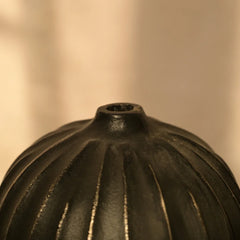 Close-up of a textured black Opus Vase against a warm beige background