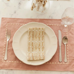 Mosaic Sand Cotton Table Napkin folded on plate over pink placemat with cutlery, top view