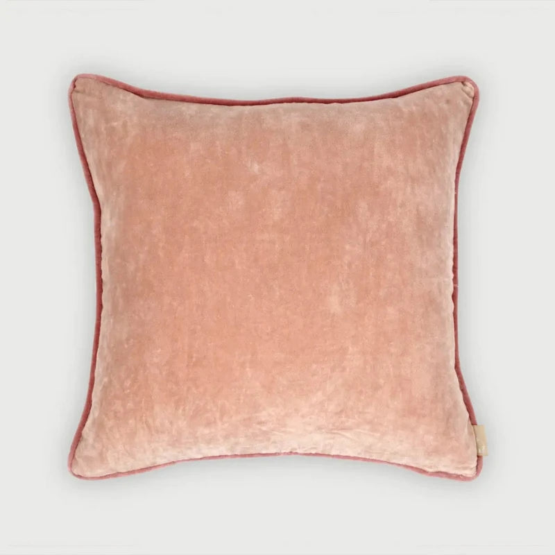 A square blush pink velvet throw pillow with a contrasting dusty rose piped border, shown against a plain light gray background.