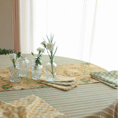 Valley Peach Linen Table Runner on striped tablecloth with glass bud vases, wide view