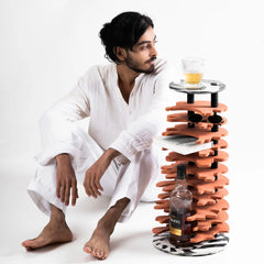 Man in white outfit sitting next to a stack of orange trays with a bottle and glass on a white background