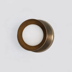 Dew Wall Sconce Small (Brass Dome) Bronze-colored circular object with a white center on a light gray background