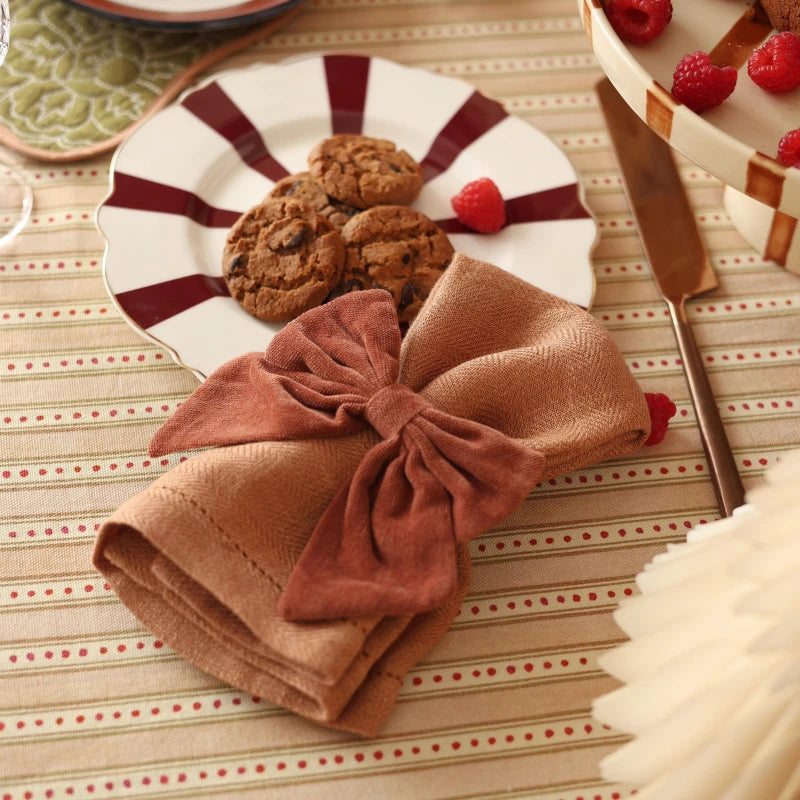 Rhubarb Velvet Napkin Ring, bow shape on napkin over striped plate with cookies, close view