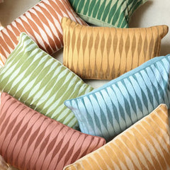 A group of decorative rectangular throw pillows with a wavy vertical stripe pattern in assorted colors, including orange, green, yellow, blue, pink, and beige, arranged together on a light neutral surface.