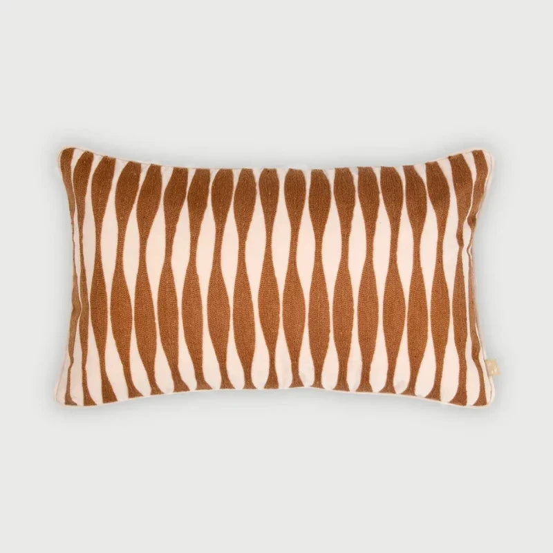A rectangular throw pillow with a vertical wavy stripe pattern in warm brown and cream, shown against a neutral light gray background.