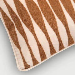 A close-up of a textured throw pillow featuring a wavy, zebra-like stripe pattern in warm brown and cream.