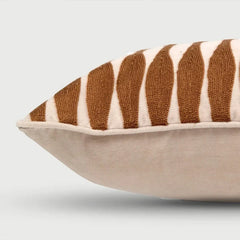 A close-up of a decorative throw pillow featuring a textured brown and cream ikat-style striped pattern on the top half and a solid cream fabric base.