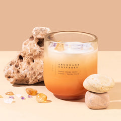 Abundant Universe Candle - Crystal Energy - Citrine Crystal, citrus ombre glass candle with citrine chips beside rock and stones