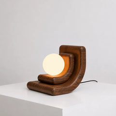 A modern wooden table lamp with a glowing oval bulb, set on a white pedestal against a light gray background.