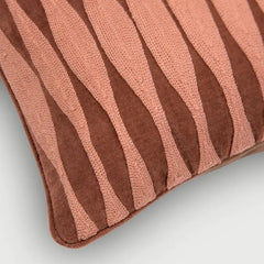 A close-up of a textured throw pillow featuring wavy vertical stripes in dusty rose pink and dark brown.