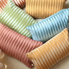 A set of decorative throw pillows with a wavy, striped pattern in multiple colors, including green, light blue, dusty pink, and mustard yellow, arranged on a neutral fabric surface.