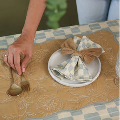 Sand Velvet Napkin Rings adjusted by hand on checked napkin and plate, high angle