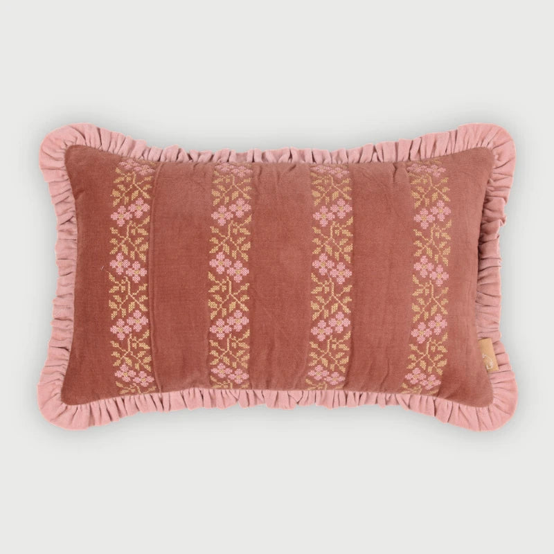A rectangular decorative throw pillow in dusty rose velvet with vertical embroidered floral stripes in pink and gold, finished with a ruffled edge, shown on a light gray background.