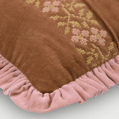 A close-up of a brown textured throw blanket with a pink ruffled edge and embroidered floral pattern in yellow and pink.