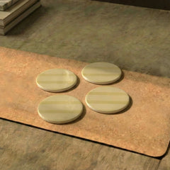 Three round metal Rayè Coasters on a brown mat with a blurred background