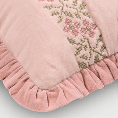 Close-up of a dusty pink decorative throw pillow with a ruffled velvet border and embroidered pink and green floral pattern.