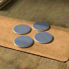 Three blue and green striped Rayè Coasters on a wooden surface