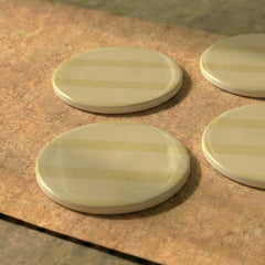 Four Rayè metal coasters with striped design on a textured surface