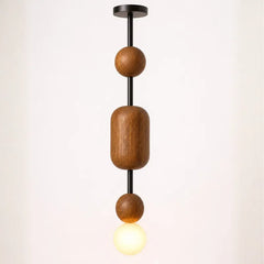 A modern pendant light fixture with three wooden geometric beads (one cylinder, two spheres) suspended on a black metal rod from a black ceiling canopy, with a glowing warm white globe bulb below.