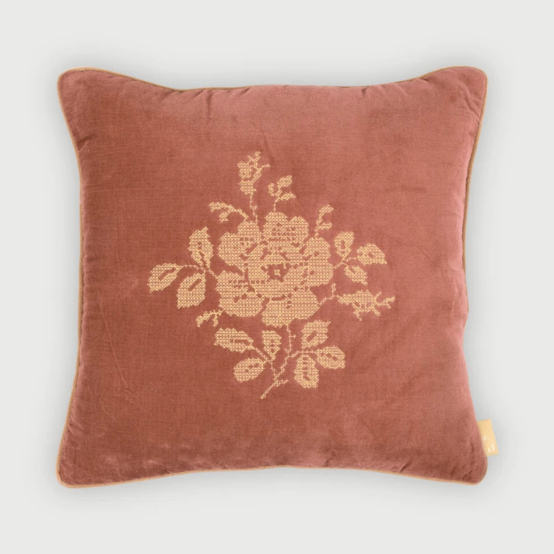 A square dusty rose velvet throw pillow featuring a beige embroidered floral motif in the center, set against a light gray background.