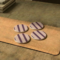 Four round metal Rayè Coasters with purple stripes on a wooden surface.