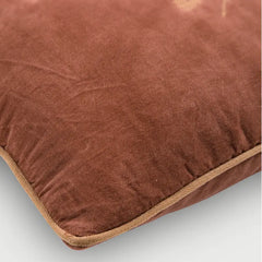 A close-up of a brown velvet throw pillow with a beige stitched edge, showing the soft texture and corner detail.