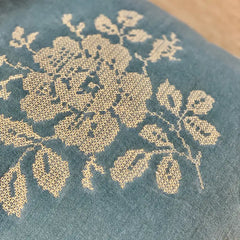 Close-up of a blue-gray fabric with a cream floral embroidery pattern.